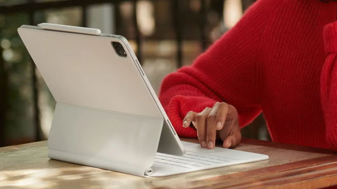 Someone in a red jumper using a white tablet connected to a foldable keyboard.