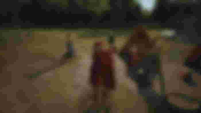 Manor Lords first person: A screenshot showing the player-character wearing noble attire and standing in a campsite populated by villagers.