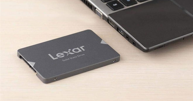 A grey, rectangular SSD with lighter grey branding on top next to a black and grey laptop.