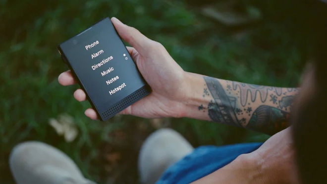 A person with a tattoo on their arm holding the new Light Phone 3 in their hand, with the main menu on-screen