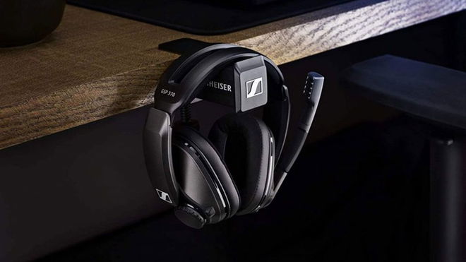 A black over-ear headset hanging from a hook attached to a brown wooden desk.