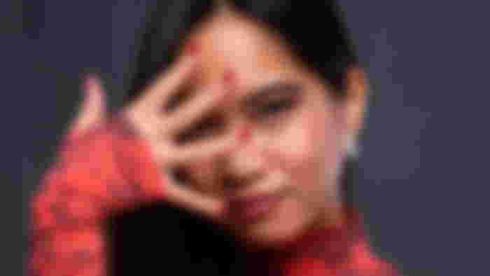 Kayane posing for a portrait covering her face with her fingers on a grey background