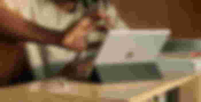 Someone using a silver iPad while propped up on a brown table by a black stand.