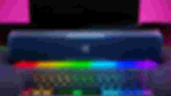 A black Razer soundbar with RGB lighting sat behind an RGB black keyboard.