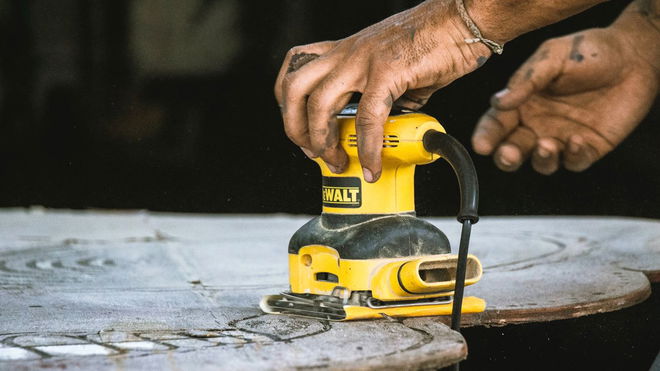 Someone using a yellow and black sander on a sheet of wood.