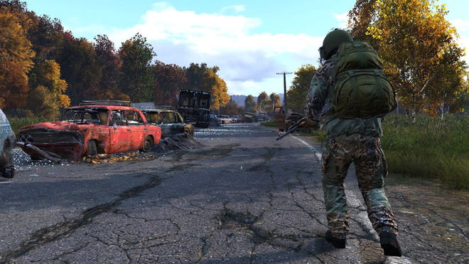 DayZ player holding gun and walking down road littered with abandoned cars