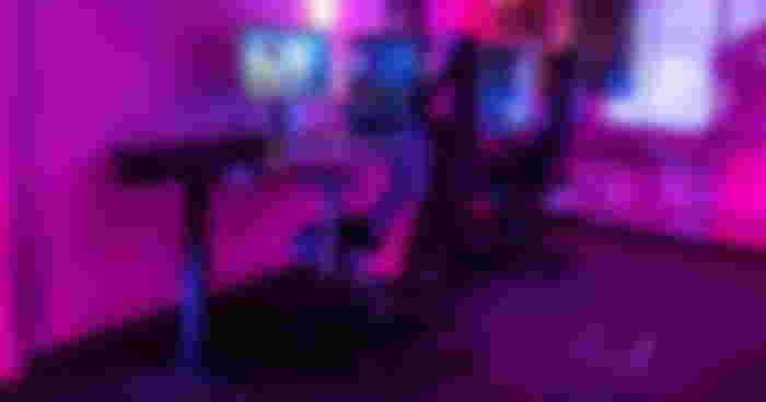 A gaming chair tucked under a desk at a PC setup, with the room bathed in pink light.