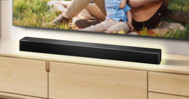 A black, rectangular soundbar with a yellow glow around it sat on a light wood cabinet below a flat screen TV on the wall.