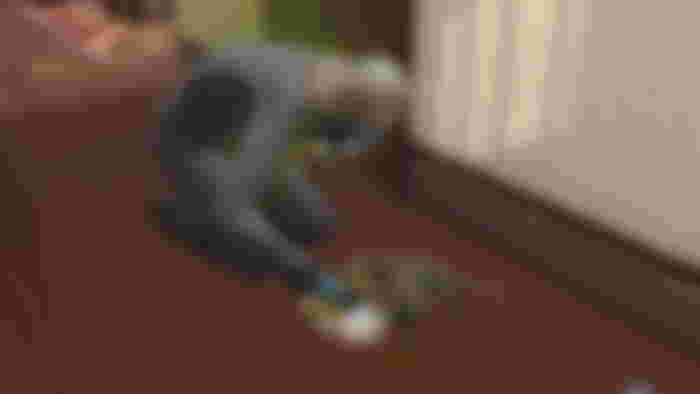 A landlord in The Sims wearing a hazmat suit cleaning mold off the floor
