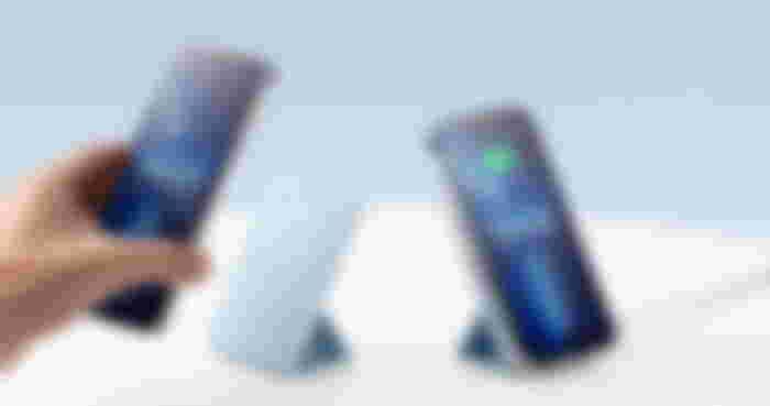 Someone placing an iPhone onto a propped-up blue magnetic charger. Next to it, an iPhone is already attached to a magnetic charger.