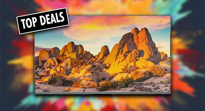A flatscreen near-framless Amazon TV with a rock arrangment bathed in the light from an orange sunset on the display. In the corner, a black and white "TOP DEALS" label.