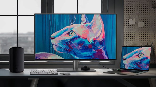 A large grey monitor with a pink and blue cat artwork on the display sat next to a laptop on a desk.